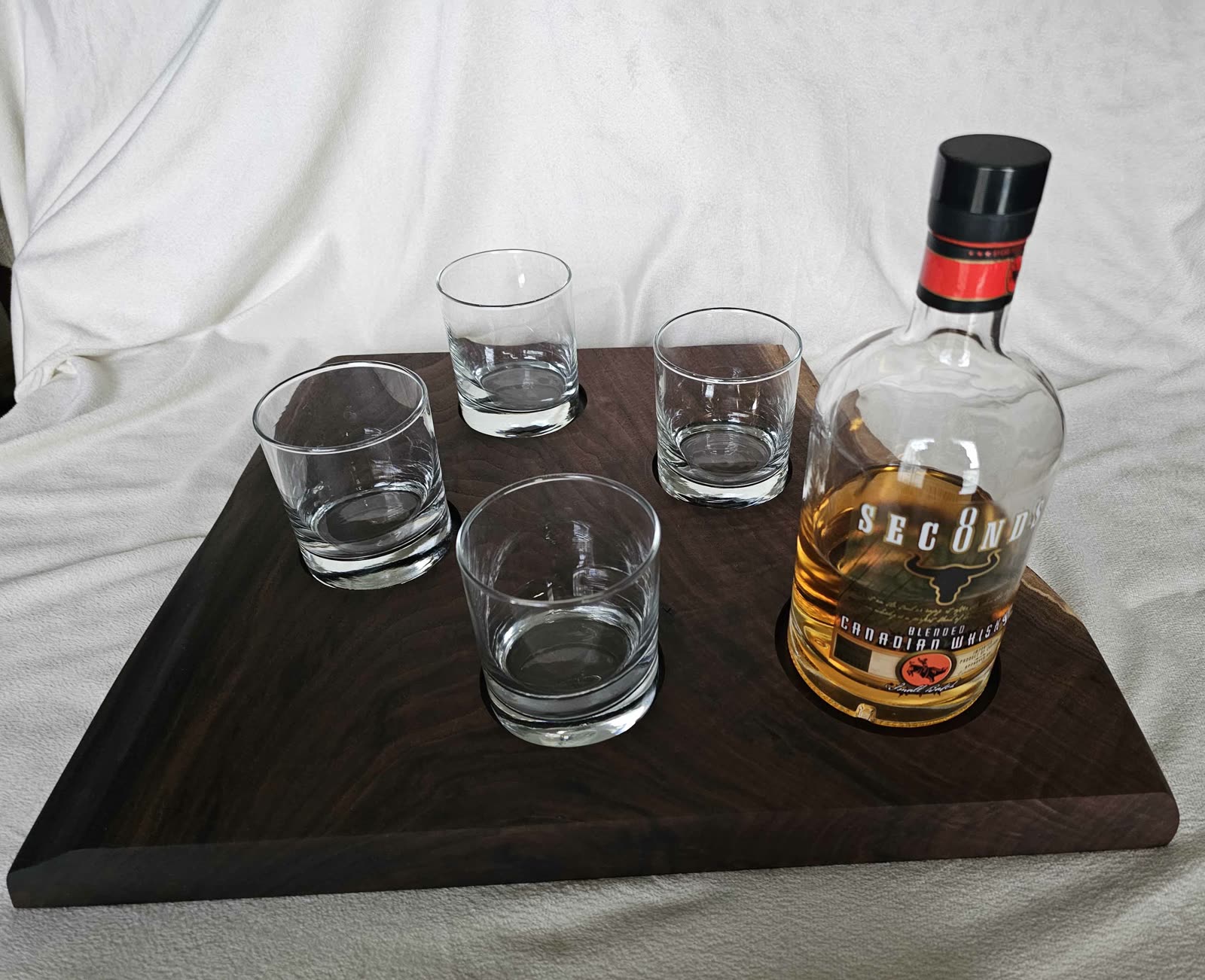 Walnut whiskey flight board with five glasses and a bottle